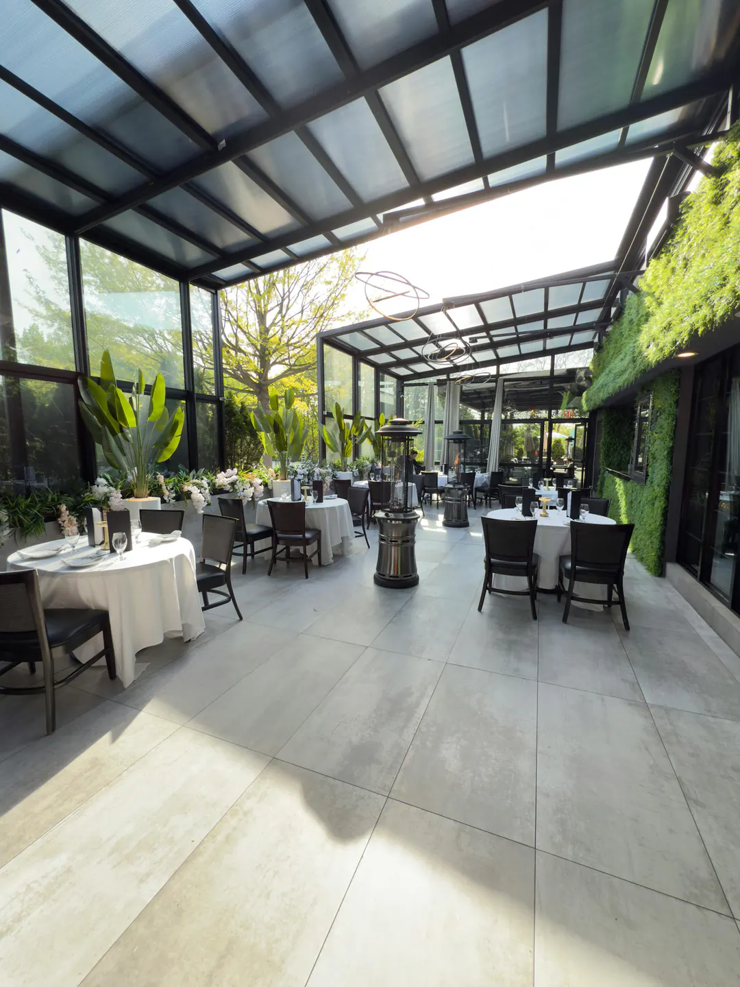 The G Room in daylight: a glass atrium over white-clothed tables, a living green wall along one side.