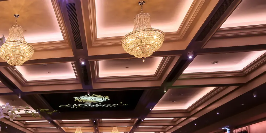 The Grand Ballroom at Mulino’s at Lake Isle: a coffered ceiling and crystal chandeliers, with the Mulino’s at Lake Isle crest lit at the center.